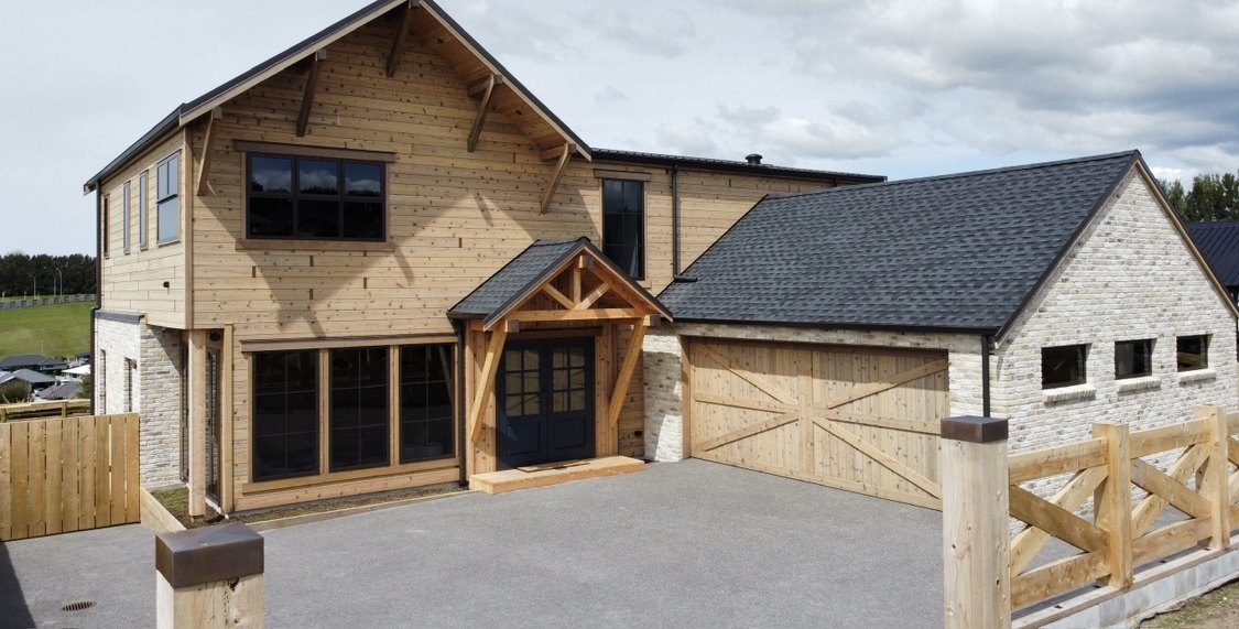 Front elevation in daylight, timber cladding, stone base and barn-style garaging